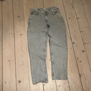 Grå jeans från Grunt med rak passform - Grå tvättade jeans från Grunt med klassisk femficksdesign och raka ben. Jeansen har normalhög midja, bälteshällor och knappgylf. Materialet är robust denim i bomull och färgen är en snygg ljusgrå nyans som passar till det mesta.