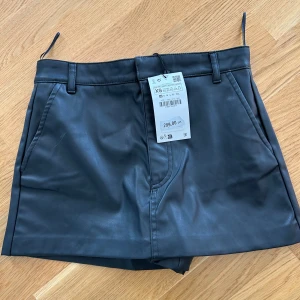 Ny Svarta skinnshorts från Zara XS  - Snygga svarta shorts i skinnimitation från  Zara De har hög midja, bälteshällor och fickor på sidorna. Perfekt för dig som vill ha en edgy och trendig look. Stängs med dragkedja och knapp framtill.