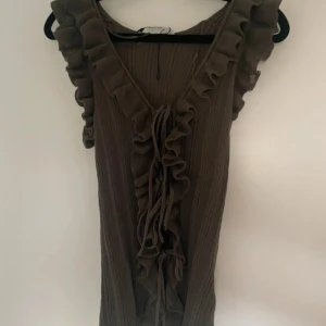 Grön zara volangtröja med knyt - Supersöt grön zara blus med volangdetaljer längs v-ringningen och knyt framtill. Klänningen har en ribbad struktur och är ärmlös, vilket ger en luftig känsla. Perfekt för dig som gillar romantiska detaljer och en avslappnad men trendig look.