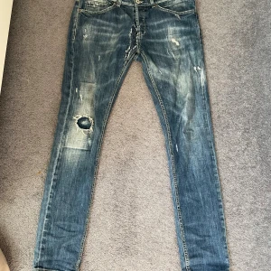 Dondup George  - Säljer ett par blå Dondup jeans med slitningar.. Jeansen är i storlek 34 men skulle säga att det passar även 33 och 32. Defekter ser ni i mitten mellan bena.