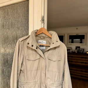Beige parkajacka med patch - Säljer en beige parkajacka från Havana med fyra stora fickor framtill, hög krage och cool patch med siffran 6 på ena ärmen. Jackan har dragsko i midjan och axelklaffar för extra stilpoäng. Perfekt för dig som gillar en avslappnad men snygg look. Passar perfekt nu inför vinter o h om du har några frågor är det bara att höra av sig🧐är en unisex jacka.