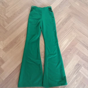Gröna bootcut byxor från FB Sister - Snygga gröna bootcut byxor från FB Sister i stretchigt material. Byxorna har hög midja och coola snörningsdetaljer vid sidorna upptill. Perfekta för dig som vill sticka ut med färg och form. Modellen är figurnära upptill och vida nertill.