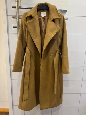 Kappa - Snygg beige kappa från H&M med klassisk krage och bälte i midjan. 2 sidofickor. 