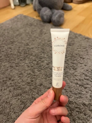 Lumene Natural Glow Primer 20ml - Lumene Natural Glow Moisturizing Illuminating Primer i en smidig tub på 20ml. Ger lyster och återfuktar huden, perfekt som bas innan smink. Tuben är vit med guldiga detaljer och har en brun kork. Vegansk formula.