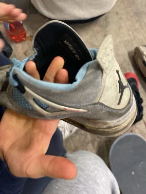 Skit Fula Jordan’s air betraktning - Nike Air Jordan 4 sneakers i grå mocka med ljusblå meshpaneler och snörning. Sulan är svart och vit med synlig luftkudde. Skon har detaljer i plast och en röd 23-logga på plösen. Perfekt för dig som gillar klassiska streetwear-vibes.