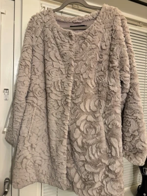 Beige pälsjacka med rosigt mönster - Säljer en fluffig beige pälsjacka med rosformat strukturmönster. Jackan har en loose passform och är långärmad, perfekt för dig som vill ha något riktigt mysigt och trendigt. Fodrad insida och stängs framtill. Superfin till höst och vinter!