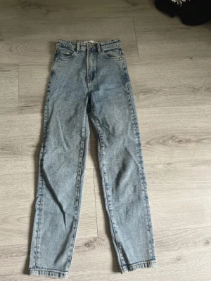 Stradivarius mom jeans ljusblå, storlek 32 - Säljer ett par ljusblå mom jeans från Stradivarius i storlek 32. Byxorna har hög midja, raka ben och klassisk femficksdesign. Tillverkade i jeansmaterial med snygg tvättad look och knappdetalj i midjan. Perfekta till sneakers eller boots.
