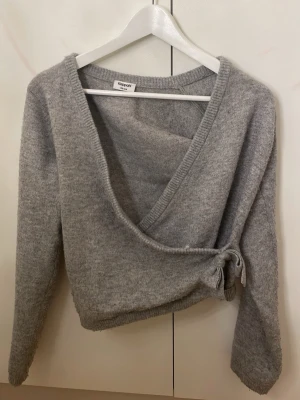 Grå omlottkofta från Kappahl - Mysig grå omlottkofta från Kappahl i mjukt stickat material. Koftan har långa ärmar, ribbade muddar och knyt i sidan för en snygg detalj. Perfekt för lager på lager under kyliga dagar. 