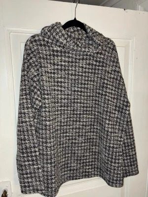 Rutig tröja med krage från Jyothi, svartvit - Säljer en svartvit rutig tröja med krage från Jyothi i storlek M. Tröjan har en hög polokrage, lång ärm och är tillverkad i ett grovt, stickat material som känns både mjukt och varmt. Perfekt för kyliga dagar och snygg till jeans eller kjol. Kommer även sälja tillhörande kjol separat.