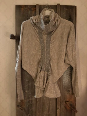 Beige stickad polotröja från HIGH use - Unik beige polotröja från HIGH use med stickade detaljer och bred polokrage. Tröjan har långärmade ribbade muddar och snyggt mönstrad panel framtill. Materialmix av alpacka, ull och polyamid ger en mjuk och lyxig känsla. Perfekt för dig som gillar coola och annorlunda plagg.