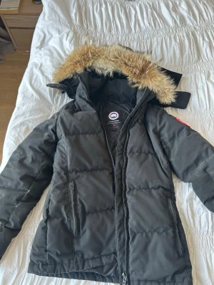  Canada Goose dunjacka med päls - Säljer en svart dunjacka från Canada Goose. Storlek XS. Jackan är lite smutsig och har en defekt på armen som syns på tredje bilden, därav priset. Säljer då jag inte använder den. 