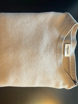 Beige stickad tröja från Kappahl - Säljer en enkel och stilren beige stickad tröja från Kappahl i storlek 158/164. Tröjan har rund hals, ribbade muddar vid ärmslut och nederkant samt långärmad passform. Perfekt för dig som gillar neutrala färger och klassisk stil.