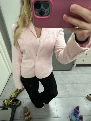 Ljusrosa kavaj med mönster - Säljer en ljusrosa kavaj med diskret mönster och klassisk krage. Kavajen har en knapp framtill och två fickor. Den är figursydd och har långa ärmar