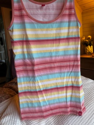 Randig linnetopp från edc - Säljer en färgglad linnetopp från edc med breda ränder i ljusblått, gult, vitt, rosa och rött. Toppen är ärmlös med rund halsringning och har mjuka kanter i rosa. Materialet är bomull, perfekt för varma dagar.