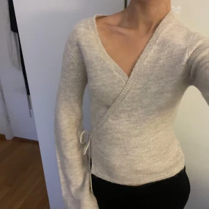 Beige omlottkofta med knyt - Mysig beige omlottkofta med knyt i sidan och v-ringad hals. 