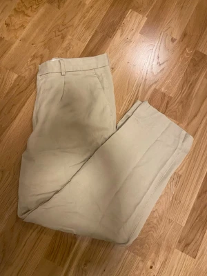 Beiga chinos från H&M  - Säljer ett par beiga chinos från H&M med relaxed fit i strl 50. Byxorna har klassisk design med bälteshällor, sidofickor och bakfickor med knapp. 