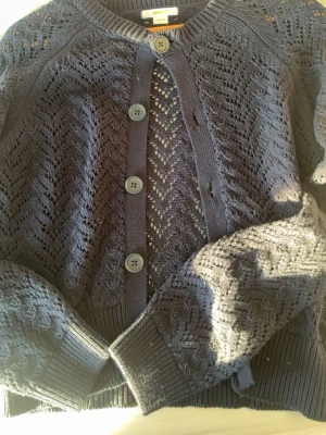 Mörkblå stickad kofta från Gina Tricot - Snygg mörkblå stickad kofta från Gina Tricot i storlek 158/164. Koftan har ett genomgående hålmönster, stora knappar framtill och ribbade muddar vid ärmslut och nederkant. Perfekt att slänga över en t-shirt för en chill look. Andvänd 1 gg💕