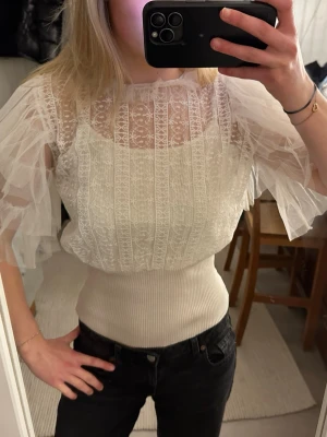 Vit spetsblus  - Supersöt vit blus med transparent spets upptill och bred ribbad midja. Puffiga volangärmar i tunn mesh ger en riktigt drömmig look. Perfekt till jeans eller kjol när du vill känna dig extra fin, köpt i Spanien så unik✨. Ingen synlig logga men känns exklusiv och trendig. Använd fåtal gånger!
