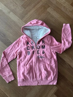 Abecrombie & fitch rosa hoodie, storlek 13/14y - Skitsnygg abecrombie hoodie/huvtröja i storlek 13-14 år. Hoodien har paljetttryck på bröstet och är fodrad med fleece på insidan. Tröjan är i mycket fint skick!