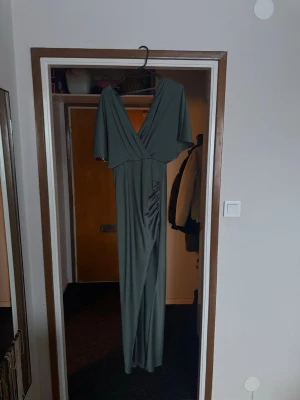 Grön långklänning med omlott och slits -  Säljer nu min älskade balklänning i storlek 36! Superfin modell och är i fint skick då jag endast burit den vid 1 tillfälle☺️ Finns lite defekter på baksidan men inget större märkbart.