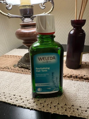 Weleda Revitalising Hair Tonic - Oanvänd. Fräsch hårtonic från Weleda med rosmarin som främjar hälsosamt hår och hårbotten. Kommer i en grön glasflaska med vit plastkork och blå etikett. Perfekt för dig som vill boosta håret med naturliga ingredienser.