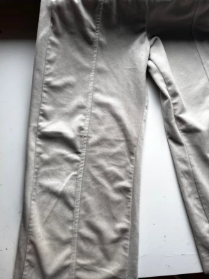 Beige mjukisbyxor från Lindex - Säljer ett par beige mjukisbyxor från Lindex i storlek 146. Byxorna har elastisk midja, raka ben och sidofickor. Materialet är mjukt och skönt, perfekt för chill dagar. Snygga sömmar längs benen ger en clean look.