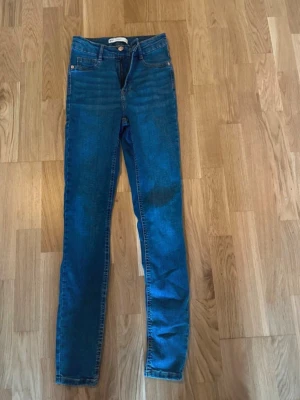 Gina tricot Molly jeans petite - Snygga blå Molly jeans petit från Gina Tricot med klassisk femficksdesign och knappstängning. Jeansen har en smal passform och är tillverkade i stretchigt denimmaterial för extra komfort. Perfekt för dig som gillar en tajt siluett och enkel stil.