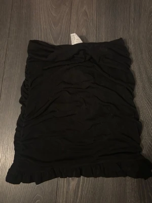 Svart volangkjol från SHEIN - Säljer en svart kortkjol från SHEIN i storlek 36/S. Kjolen har volangdetalj längst ner och är gjord i mjukt polyester-material med lite stretch. Enkel och snygg design som är lätt att matcha med olika toppar. Aldrig använd