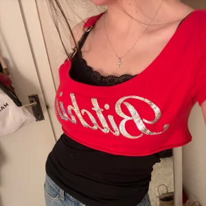 Röd croppad oneshoulder topp Fashion Nova - Säljer en röd croppad oneshoulder topp från Fashion Nova med glittrigt silvrigt tryck på framsidan. Toppen har metallringar vid axeln och är tillverkad i mjukt bomullsmaterial. Perfekt för dig som vill sticka ut med en edgy stil. Den sitter mot kroppen på mig men tror den ska sitta lite lösare. Strl står ej men troligen XXS/XS. Mycket bra skick o använd en gång av mig men köpt second hand.❣️🖇️