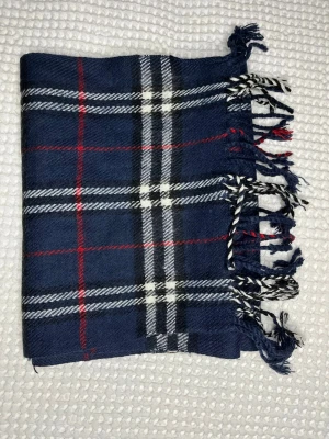 Mörkblå rutig halsduk med fransar burberry - Klassisk halsduk i mörkblått med rutigt mönster i vitt, svart och rött. Halsduken har tvinnade fransar i ändarna och är tillverkad i ett mjukt tyg som känns skönt mot huden. Perfekt accessoar för att lyfta din outfit med en tidlös look.