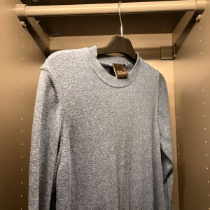 Blå stickad  merinoulltröja från Oscar Jacobson  - Snygg blå stickad tröja från Oscar Jacobsson med rund halsringning och långa ärmar. Tröjan har en enkel och stilren design, perfekt att matcha med jeans.