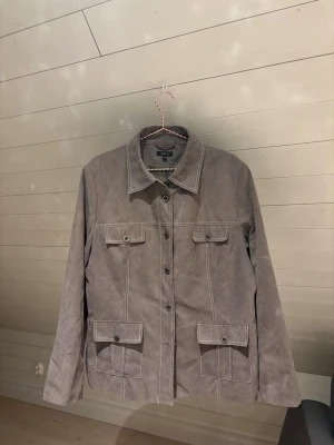 Grå skinnjacka - Snygg grå skinnjacka med fyra fickor framtill och markerade sömmar. Klassisk krage och knäppning med knappar hela vägen. 