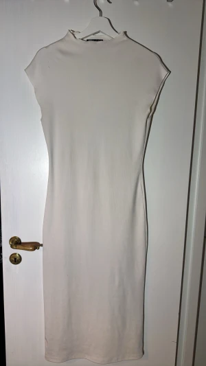 Vit ribbad långklänning från Zara - Säljer en stilren vit långklänning från Zara i ribbat material. Klänningen har hög hals, är ärmlös och har en kroppsnära passform som framhäver siluetten. Perfekt för dig som gillar minimalistisk och modern stil. Finns fläckar som jag absolut tror kan gå bort med tuffare fläckborttagning.