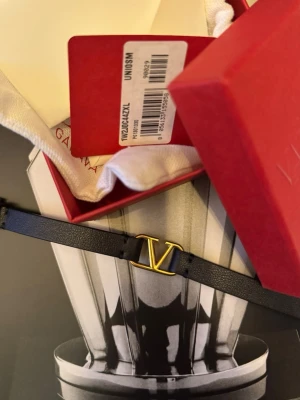 Valentino svart läderarmband - Snyggt svart armband i läder från Valentino med ikoniskt guldfärgat V-spänne. Kommer i original röd ask och med tygpåse. Perfekt accessoar för dig som gillar stilrena detaljer och exklusiv känsla.