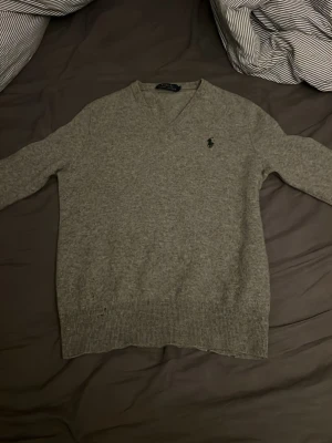 Kashmir polo Ralph Lauren tröja - Säljer en stilren grå v-ringad tröja från Polo Ralph Lauren med den klassiska broderade loggan på bröstet. Tröjan är i mjuk kashmir har och ribbade muddar. Perfekt för lager-på-lager under hösten och vintern.