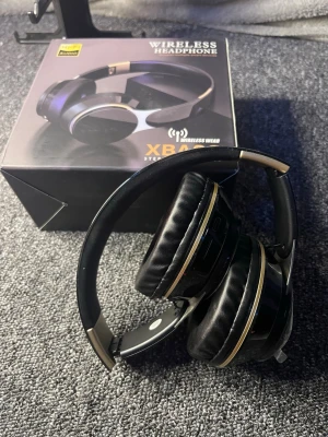 Svarta trådlösa over-ear hörlurar - Snygga svarta trådlösa over-ear hörlurar från XBA med gulddetaljer. De har vadderade öronkuddar och justerbart huvudband för extra komfort. Perfekta för musik, gaming eller videos. Bluetooth-anslutning och hopfällbar design gör dem smidiga att ta med.