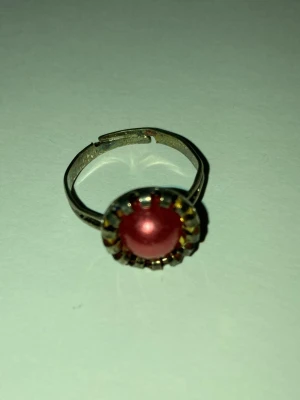 Två färgglada justerbara ringar - Säljer två coola ringar: en med en rund röd pärla i guldfärgad infattning och en rosa ring med ett lila hjärta. Båda är justerbara och har en lekfull design som sticker ut. Perfekta accessoarer för dig som gillar färg och unika smycken. Frakt är 22-100kr beroende på vikten. Kontakta mig om du har frågor eller vill köpa.