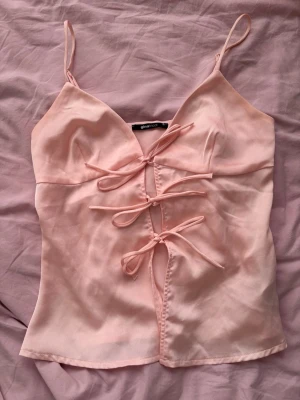Ljusrosa linnetopp med snörning - Supersöt ljusrosa linnetopp från Gina Tricot med tunna axelband och snörning framtill. Toppen har en feminin v-ringning och är tillverkad i ett mjukt, silkesliknande material. Perfekt för att lyfta vilken outfit som helst!