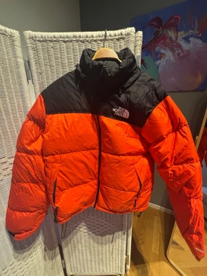 Röd och svart dunjacka The North Face - Säljer en riktigt fet röd och svart dunjacka från The North Face. Jackan har hög krage, dragkedja framtill och två sidofickor. Klassisk pufferstil med stora paneler och logga på bröstet. Perfekt för kalla dagar när du vill hålla stilen.