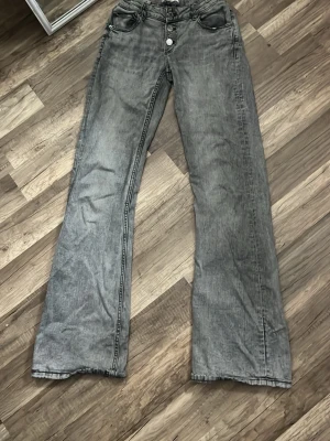 Gråa low waist flare jeans med knappar - Säljer ett par gråa jeans med flare ben och flera knappar i gylfen. Jeansen har klassisk femficksdesign och är tillverkade i ett mjukt denimtyg. Perfekta för dig som gillar Stockholmsstil och trendig stil.