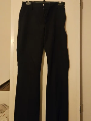 Svarta vida kostymbyxor - Säljer ett par svarta kostymbyxor med vida ben och klassisk passform. Byxorna har hällor för skärp, fickor fram och bak samt stängs med dragkedja och knapp. Från bikbok.