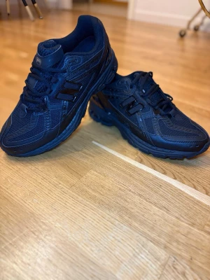 Svarta New Balance sneakers - Snygga svarta sneakers från New Balance med sportig design. Skorna har mesh- och syntetdetaljer, klassisk snörning och en robust sula som ger bra grepp. Perfekta för dig som gillar streetstyle och vill ha bekväma skor med cool look.