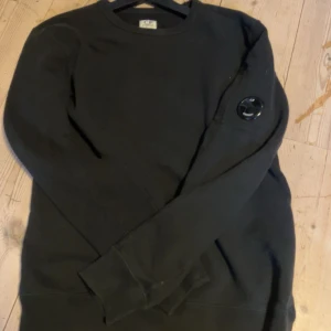 Svart sweatshirt från C.P. Company - Det här är en snygg svart cp company sweatshirt.Tröjan har ingen exakt storlek i sig men passar mig perfekt som är 170 cm lång. Tröjan har en liten repa på badgen men ingen synligt om man inte kollar noggrant. Tröjan har använts typ 2-3 gånger så nästan helt oanvänd. Jag säljer den här tröjan eftersom den mest samlar damm men inget fel på tröjan. Finns även Qr kod för att kolla att den är autentiskt. Dm om ni har frågor pris kan diskuteras.
