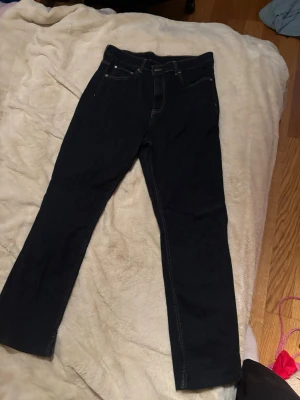 Mörkblå raka jeans med kontrastsömmar - Snygga mörkblå jeans med raka ben och kontrastsömmar. Klassisk femficksmodell och knappgylf. Perfekta till vardags för en clean och enkel look.