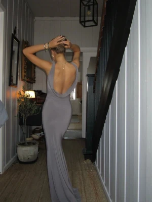 Lång taupe klänning från Design Si - Supersnygg långklänning i taupe från Design Si. Klänningen har en tight passform, öppen rygg och draperad urringning både fram och bak. Tillverkad i ett glansigt, stretchigt material som ger en lyxig känsla. Perfekt för dig som vill sticka ut med en elegant och modern look. Den är i storleken xs/s och har aldrig använts.