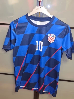 Modrić  - Snygg blå fotbollströja med rutigt mönster i mörkblått och blått, röda diagonala linjer och Kroatiens landslagsemblem på bröstet. Nummer 10 och namnet Modrić tryckt på ryggen. Perfekt för fotbollsfans! Den är oanvänd men den är tvättad. Tveka inte för att ställa frågor! Priset är inte hugget i sten.
