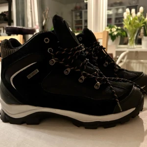 Svarta kängor med snörning - Svarta kängor med grov sula och snörning. Skorna har detaljer i vitt och reflekterande material samt metallhål för snören. Aldrig använda pga felköp. Strl 44.