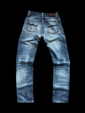 Nudie Jeans Steady Eddie Dry - Modell Steady Eddie Org Tonal Dry (Blåa detaljer på backfickan). Köpta ca 2010 i butik och använda väl (15+ år!). Har lagats flera gånger i butik. Väldigt fina fades och slitningar  W30/L36 Yb-längd 110cm Ib -längd 80cm Benöppning 17cm Midja 39cm Lår 25,5cm  Skicka DM för fler bilder/funderingar.