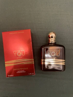 Emporio Armani Stronger With You Amber - Exklusiv parfym från Emporio Armani, Stronger With You Amber. Flaskan är mörkbrun med gulddetaljer och rundad form, och har en elegant guldfärgad kork. Förpackningen är röd med guldtext och matchande detaljer. Innehåll: 100 ml .