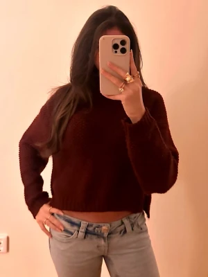Mörkröd cropped stickad tröja - Snygg mörkröd stickad tröja i cropped modell med långa ärmar och ribbade muddar. Perfekt till jeans för en avslappnad och trendig look. Mjuk och skön, passar perfekt till kyligare dagar.